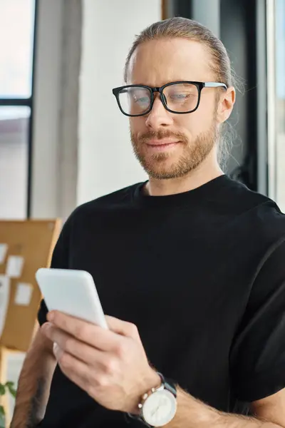 Homme d'affaires élégant en t-shirt noir et lunettes naviguant sur Internet sur smartphone au bureau — Photo de stock