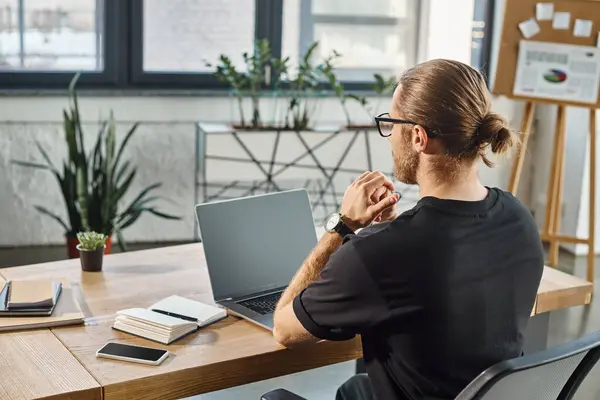 Back view of manager in black t-shirt near laptop with blank screen on work desk in modern office — Stock Photo