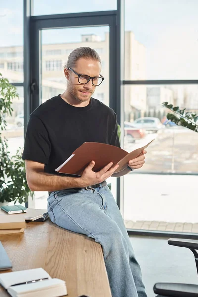 Businessman in eyeglasses sitting on work desk and looking in folder with documents in office — Stock Photo