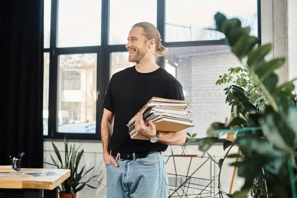 Happy manager in casual attire holding pile of notebooks while looking away in modern office — Stock Photo