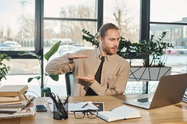 L'uomo d'affari elegante che gesticola vicino a computer portatile mentre ha videochiamata su computer portatile a posto di lavoro in ufficio — Foto stock