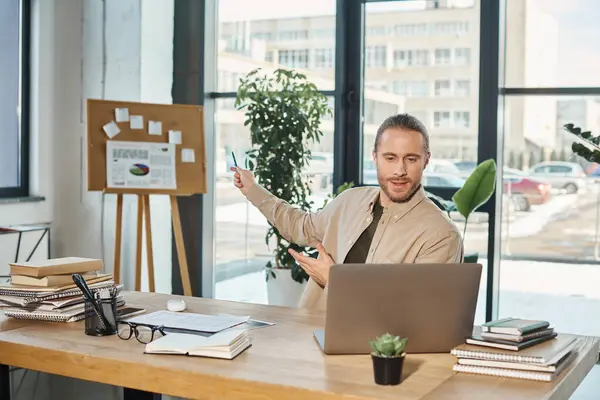 Gestionnaire d'entreprise pointant vers flip chart avec des graphiques lors d'une réunion vidéo sur ordinateur portable dans le bureau moderne — Photo de stock