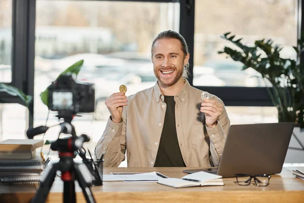 Счастливый амбициозный бизнесмен показывает биткоины и записывает видео блог на цифровую камеру в офисе — стоковое фото