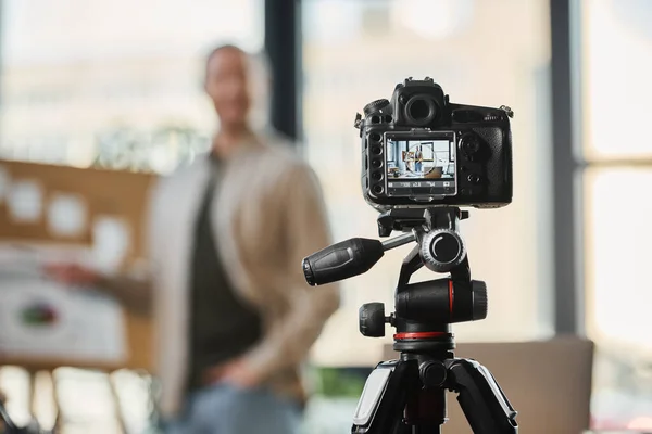Selective focus on digital camera near blurred businessman recording video blog in modern office — Stock Photo