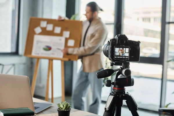 Fokus auf Digitalkamera und Laptop in der Nähe verschwommener Geschäftsleute, die Videoinhalte im Büro aufzeichnen — Stockfoto