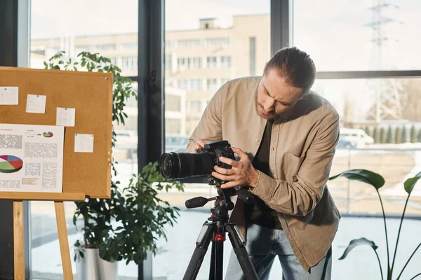 Бизнесмен в повседневной одежде регулирует цифровую камеру возле флип-чарта с инфографикой в офисе — стоковое фото