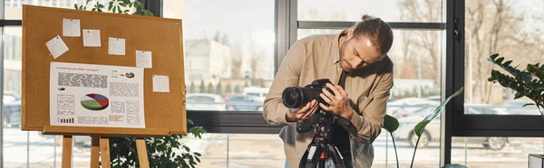 Manager in Freizeitkleidung justiert Digitalkamera in der Nähe Flipchart mit Grafiken im Büro, Banner — Stockfoto