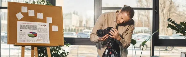 Gerente em traje casual ajustando câmera digital perto de flip chart com gráficos no escritório, banner — Fotografia de Stock