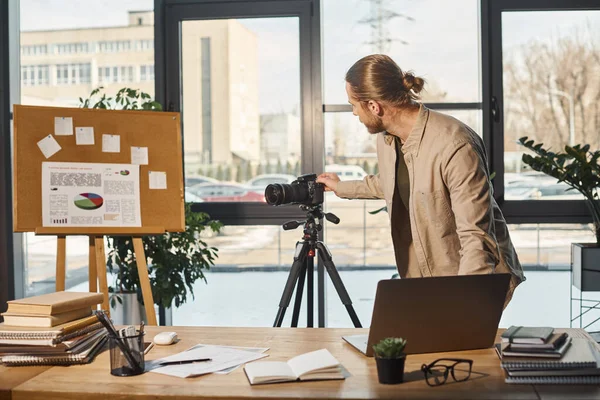 Firmenchef justiert Digitalkamera auf Stativ in der Nähe von Flipchart mit Diagrammen und Bürotisch — Stockfoto