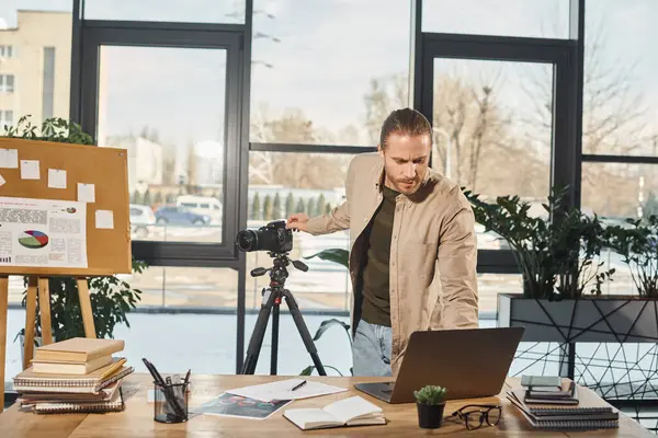 Gerente en traje casual ajuste portátil y cámara digital cerca del escritorio en la oficina, video blogger - foto de stock