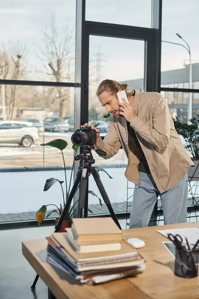 Homme d'affaires parler sur smartphone et ajuster l'appareil photo numérique à côté du bureau dans le bureau moderne — Photo de stock
