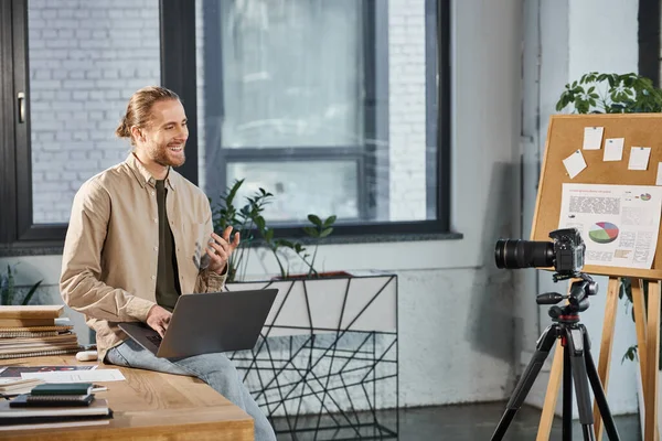 Zufriedener Manager mit Laptop am Schreibtisch vor der Digitalkamera im modernen Büro — Stockfoto