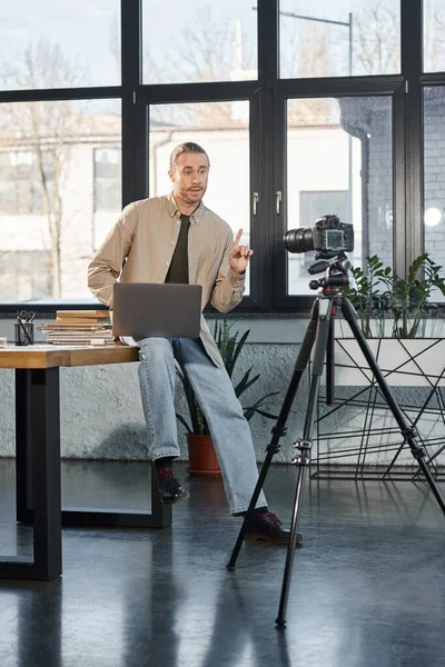 Homme d'affaires assis sur le bureau avec ordinateur portable et parler devant un appareil photo numérique, blog vidéo — Photo de stock
