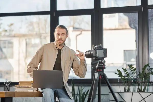 Креативный бизнесмен с ноутбуком говорит и жестикулирует перед цифровой камерой в офисе — стоковое фото