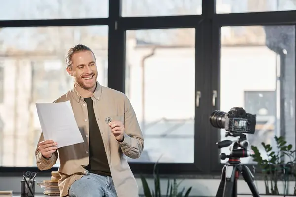 Entrepreneur souriant tenant Bitcoin et document devant l'appareil photo numérique dans le bureau moderne — Photo de stock