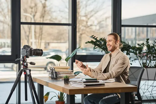 Веселый бизнесмен разговаривает и жестикулирует перед цифровой камерой на рабочем столе с ноутбуками — стоковое фото