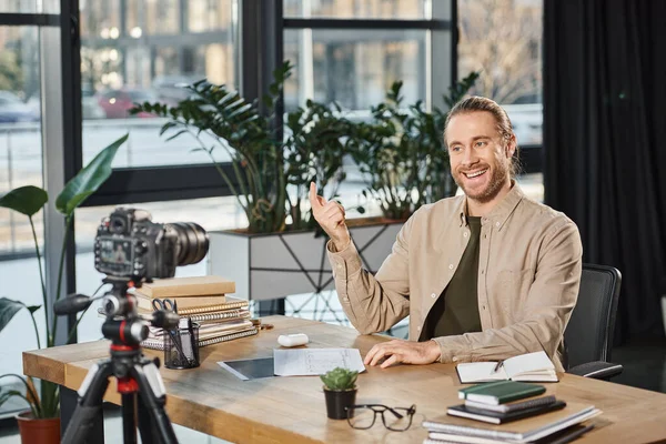 Happy successful businessman talking and gesturing during video blog at work desk with notebooks — Stock Photo