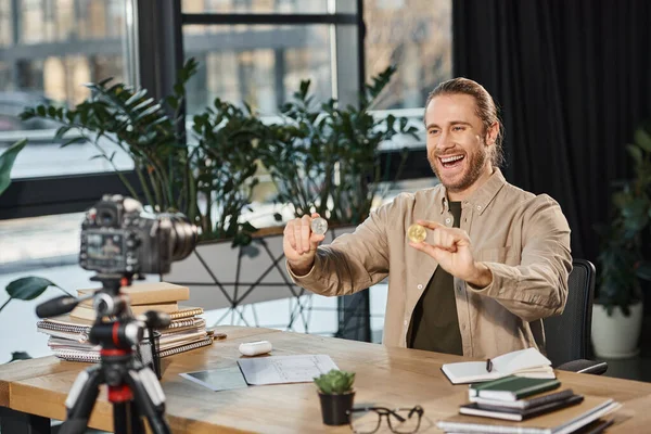 Overjoyed creative businessman holding bitcoins in front of digital camera at work desk in office — Stock Photo