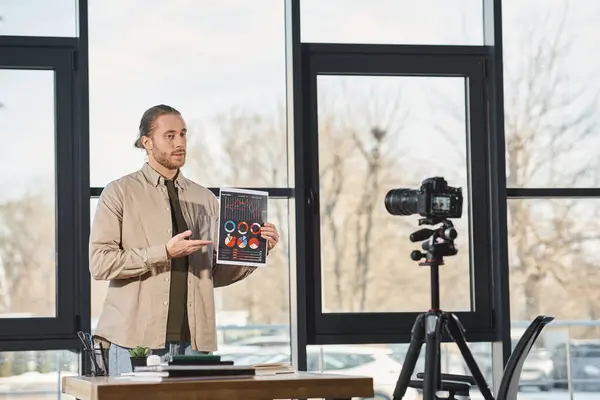 Empresário mostrando documento com infográficos durante vídeo blog em câmera digital no escritório — Fotografia de Stock