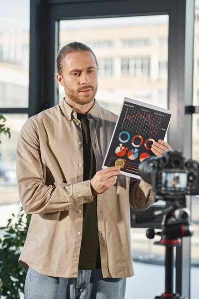 Confident manager showing paper with graphs and recording video blog on digital camera in office — Stock Photo