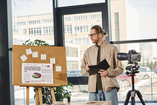 Manager mit Notizbuch schaut bei Videopräsentation im modernen Büro auf Korkboard mit Grafiken — Stockfoto