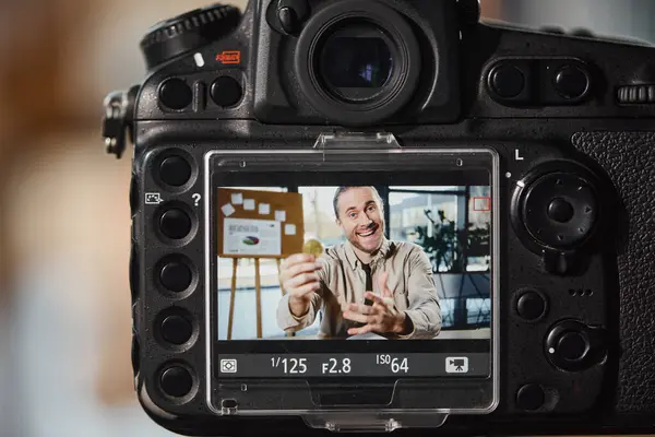Close up of digital camera near excited entrepreneur recording video blog at workplace in office — Stock Photo