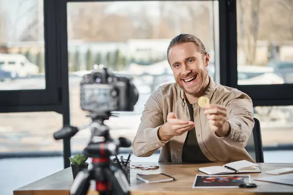 Joyful successful entrepreneur showing bitcoin at digital camera and recording video blog in office — Stock Photo