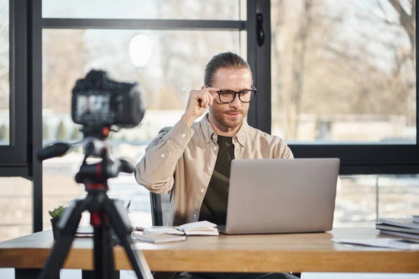 Selbstbewusster Geschäftsmann mit Brille blickt im modernen Büro auf Laptop vor Digitalkamera — Stockfoto