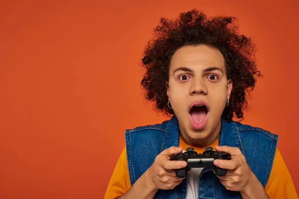 Attraente africano americano uomo in abbigliamento casual emotivamente giocare video giochi su sfondo arancione — Foto stock