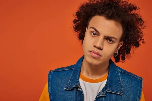 Atractivo joven afroamericano hombre en traje urbano casual posando emocionalmente sobre fondo naranja - foto de stock