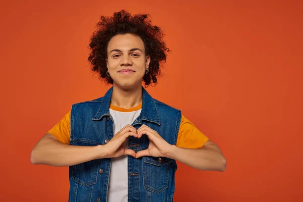 Beau homme afro-américain en tenue urbaine décontractée posant émotionnellement sur fond orange — Photo de stock