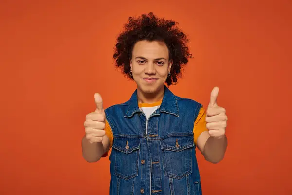 Guapo joven afroamericano hombre en traje urbano casual posando emocionalmente sobre fondo naranja - foto de stock