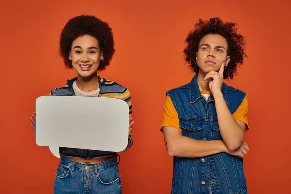 Young african american siblings in casual attire posing with speech bubble on orange backdrop — Stock Photo
