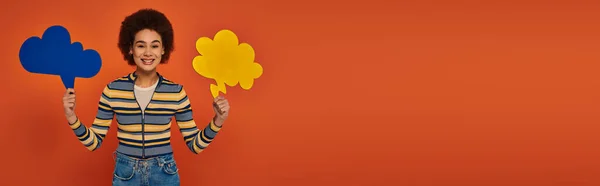 Jolie femme américaine africaine posant avec des bulles de pensée bleues et jaunes sur fond orange, bannière — Photo de stock