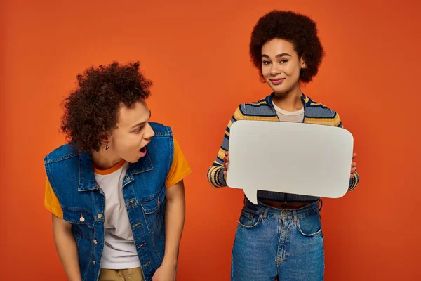 Emocional joven afroamericano hermano y hermana posando con burbuja del habla sobre fondo naranja - foto de stock