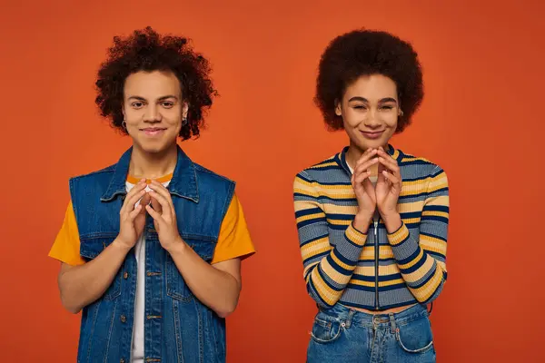 Jóvenes y atractivos hermanos afroamericanos posando juntos y haciendo gestos animados sobre fondo naranja - foto de stock