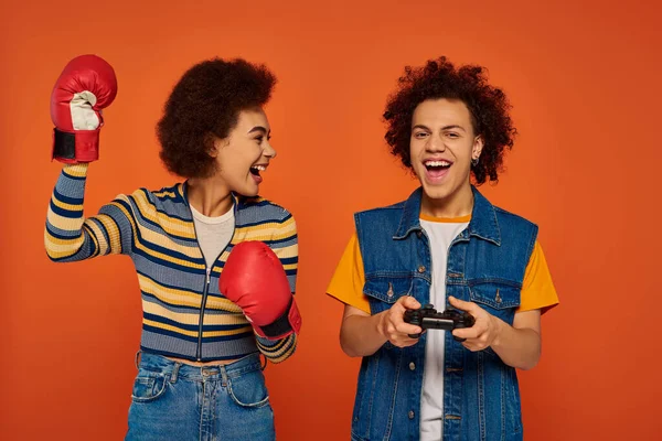 Cheerful african american woman in boxing gloves posing next to her brother with joystick, family — Stock Photo