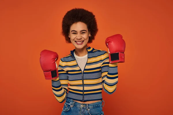 Beautiful jolly african american woman posing actively with boxing gloves on orange backdrop — Stock Photo