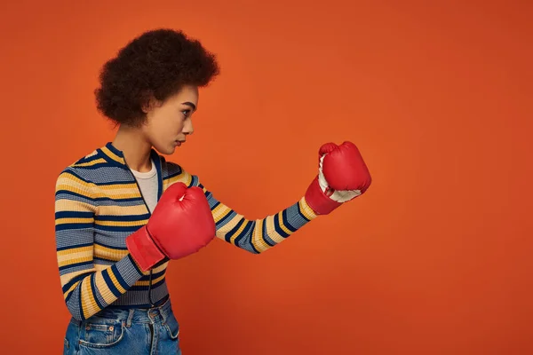 Schöne sportliche afrikanisch-amerikanische Frau posiert aktiv mit Boxhandschuhen auf orangefarbenem Hintergrund — Stockfoto