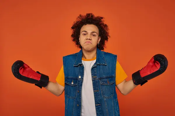 Confused sporty african american male model posing lively in boxing gloves on orange background — Stock Photo