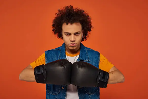 Good looking sporty african american man posing actively in boxing gloves on orange background — Stock Photo