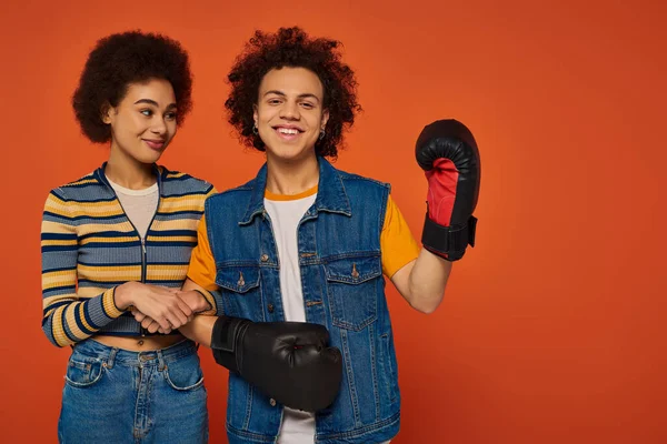 Joyous african american man in boxing gloves having fun with his sister on orange backdrop, family — Stock Photo