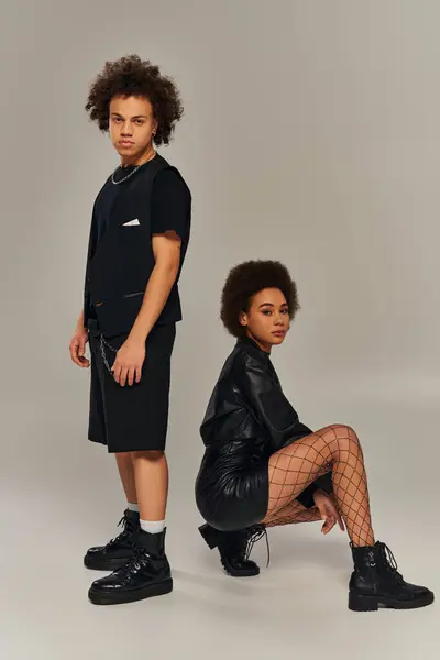 Attrayant frère afro-américain et soeur en tenues noires accroupi sur fond gris — Photo de stock