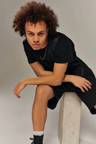 Atractivo modelo masculino afroamericano en traje urbano negro posando activamente sobre fondo gris - foto de stock