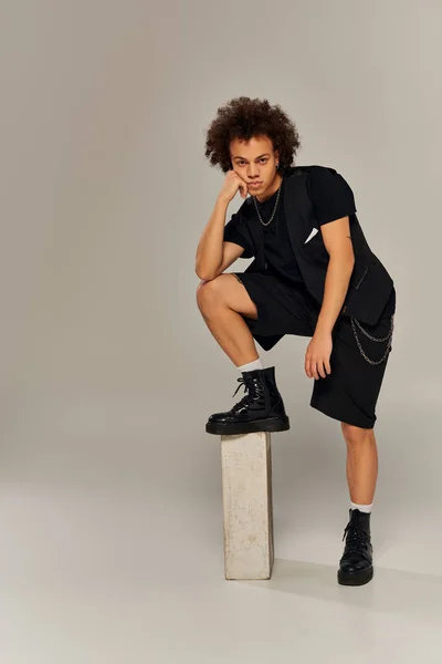 Appealing african american male model in black urban stylish attire posing actively on gray backdrop — Stock Photo