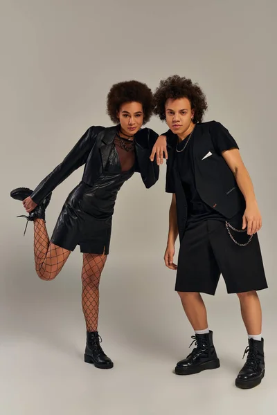 Souriant jeune frère afro-américain et soeur en vêtements urbains posant ensemble sur fond gris — Photo de stock
