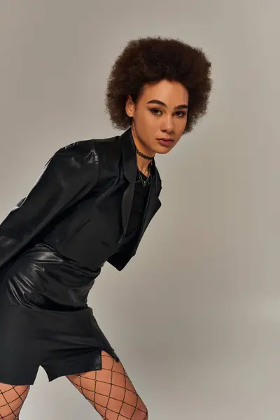 Привлекательная африканская американка в черном, с сетчатыми колготками, позирующая на сером фоне — стоковое фото