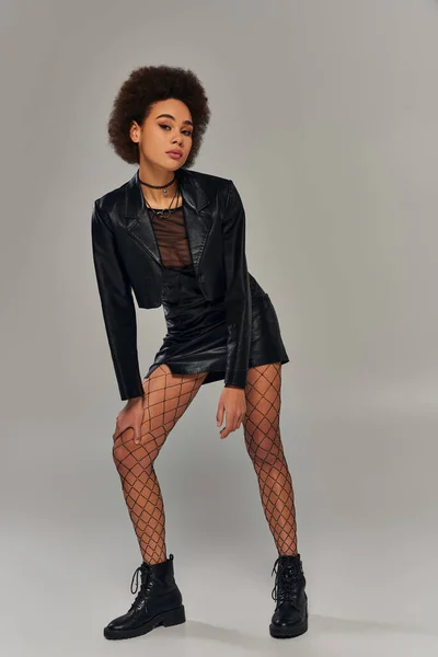 Alluring african american woman in stylish black attire with fishnet tights posing actively — Stock Photo