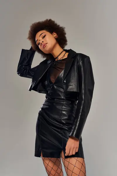 Atractiva mujer afroamericana en elegante traje negro con medias de rejilla posando activamente - foto de stock