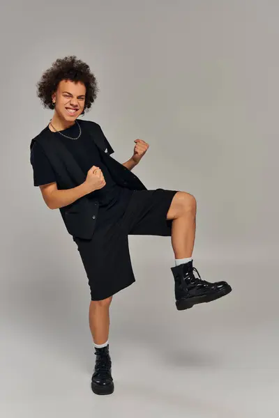 Cheerful african american male model in black urban stylish attire posing actively on gray backdrop — Stock Photo